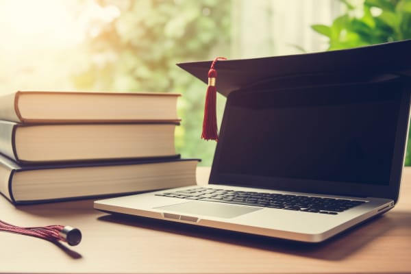 Laptop with a graduation cap on its screen beside a stack of books, symbolizing strategies for CKA certification success.