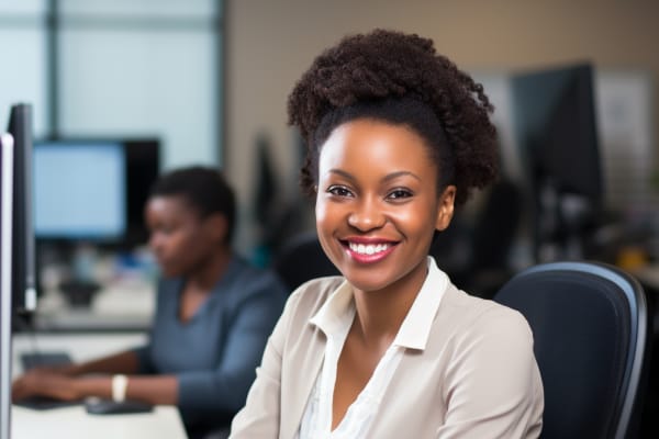 IT Support Classes. A cheerful young woman with a bright smile working at her desk in an office environment.